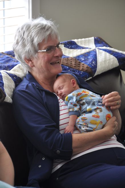 A picture of Mason in his grandmother's arms with the baby quilt on the couch behind them.